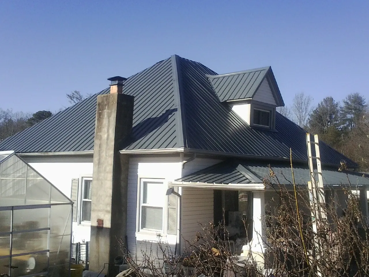 Dark blue standing seam metal roof on a white farmhouse with dormer — Slate & Tile Roof Repair by Roofing Brothers in Ford