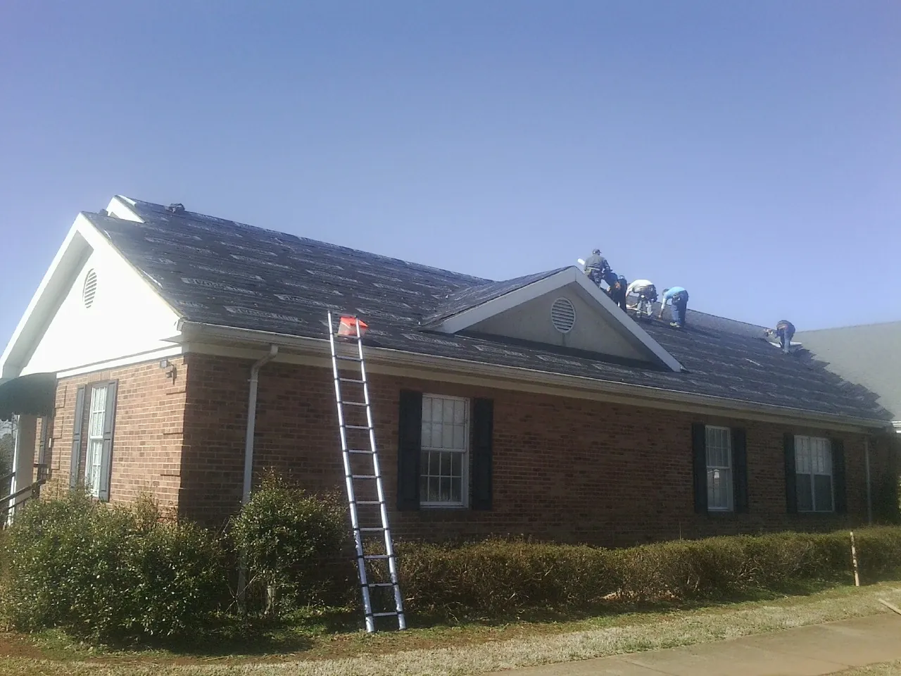 Crew tearing shingles off a brick ranch roof with a ladder set — Metal Roof Repair work by our crew in Ford