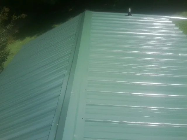New green metal panels meeting at the ridge of a roof — Flat Roof Repair work by our crew in Ford