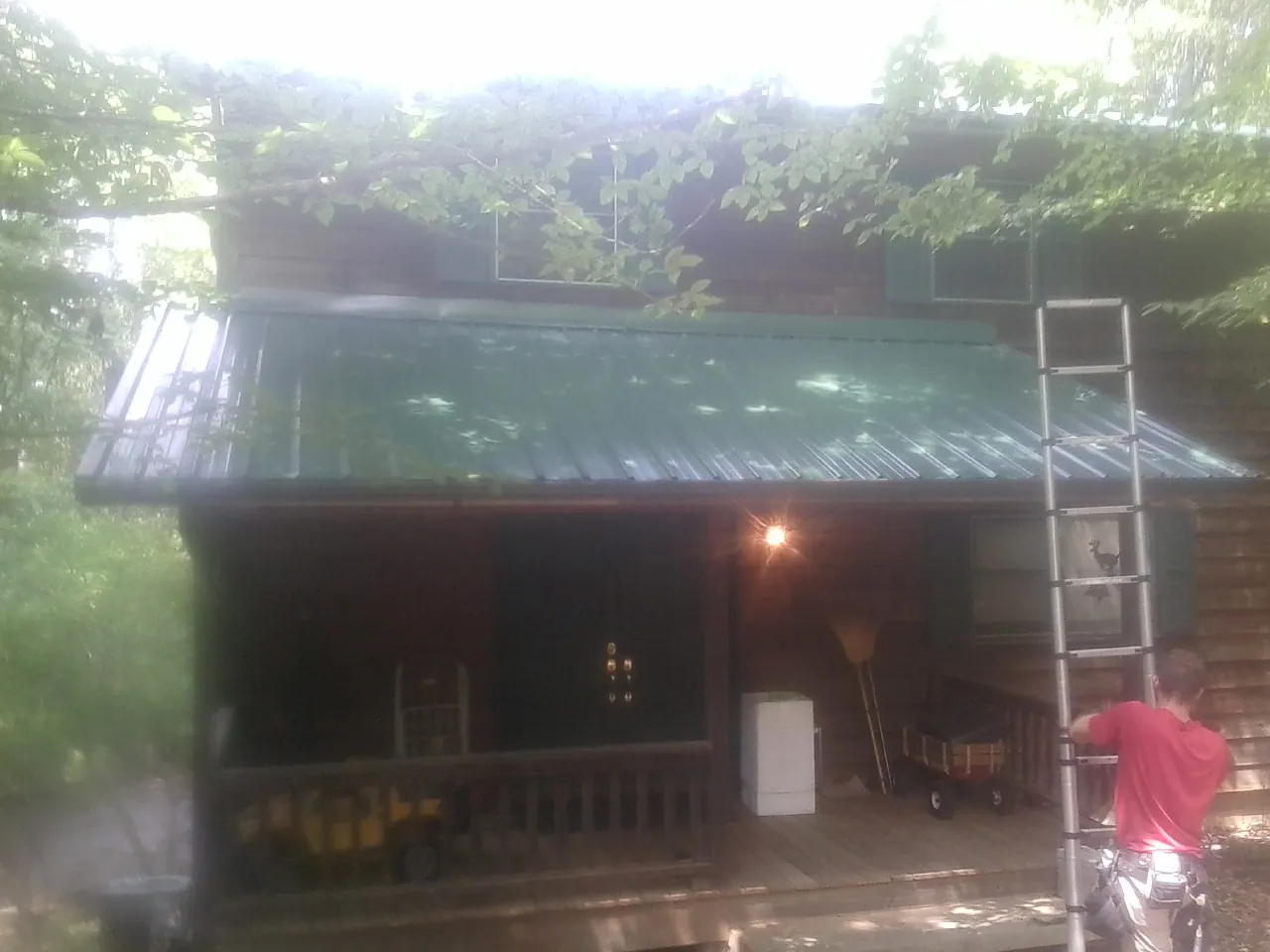 Worker on a ladder at the green porch roof of a wooded cabin in Ford