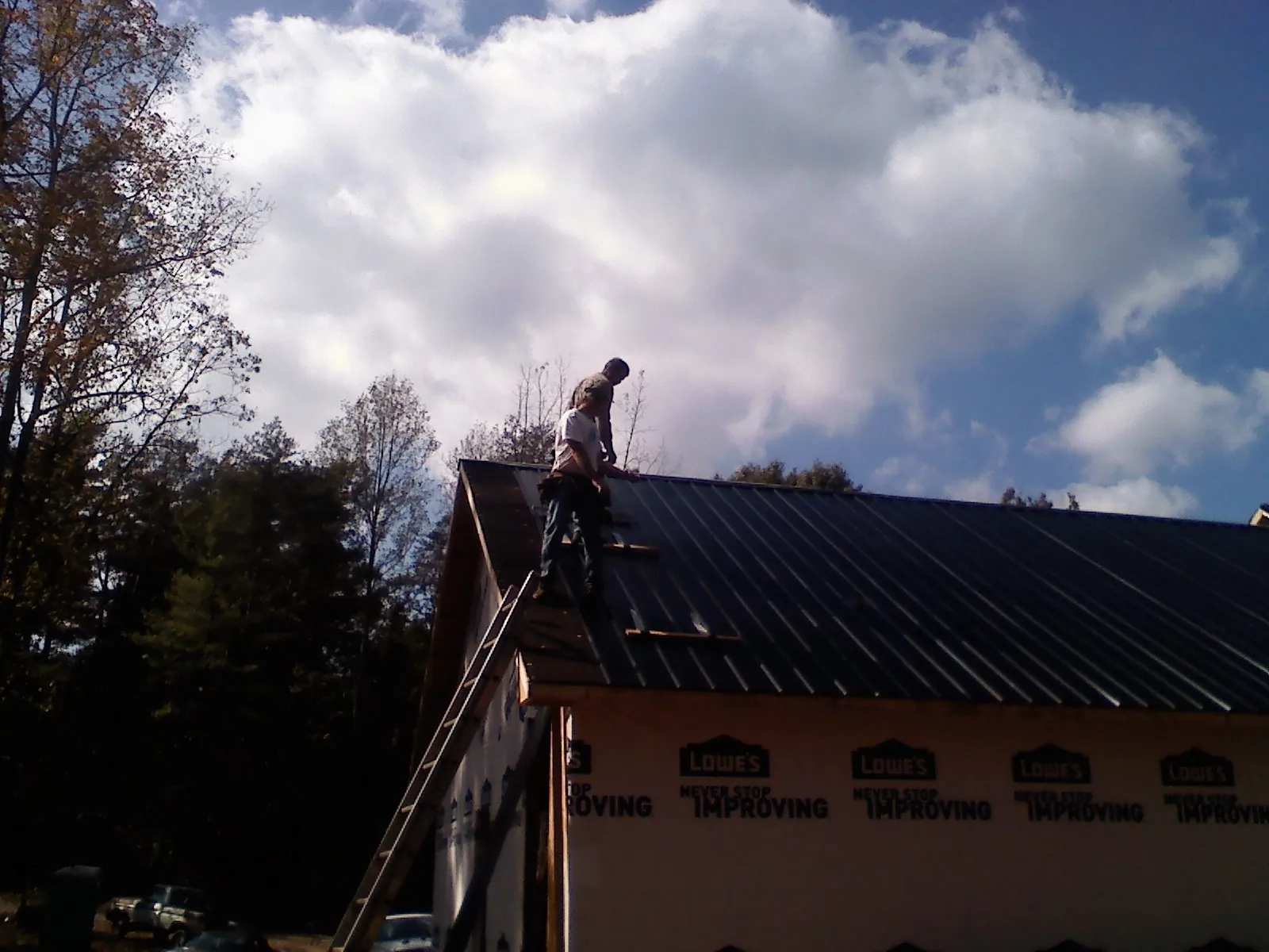 Roofer fastening dark metal panels high against a cloudy sky, from a Roof Inspection job in Ford