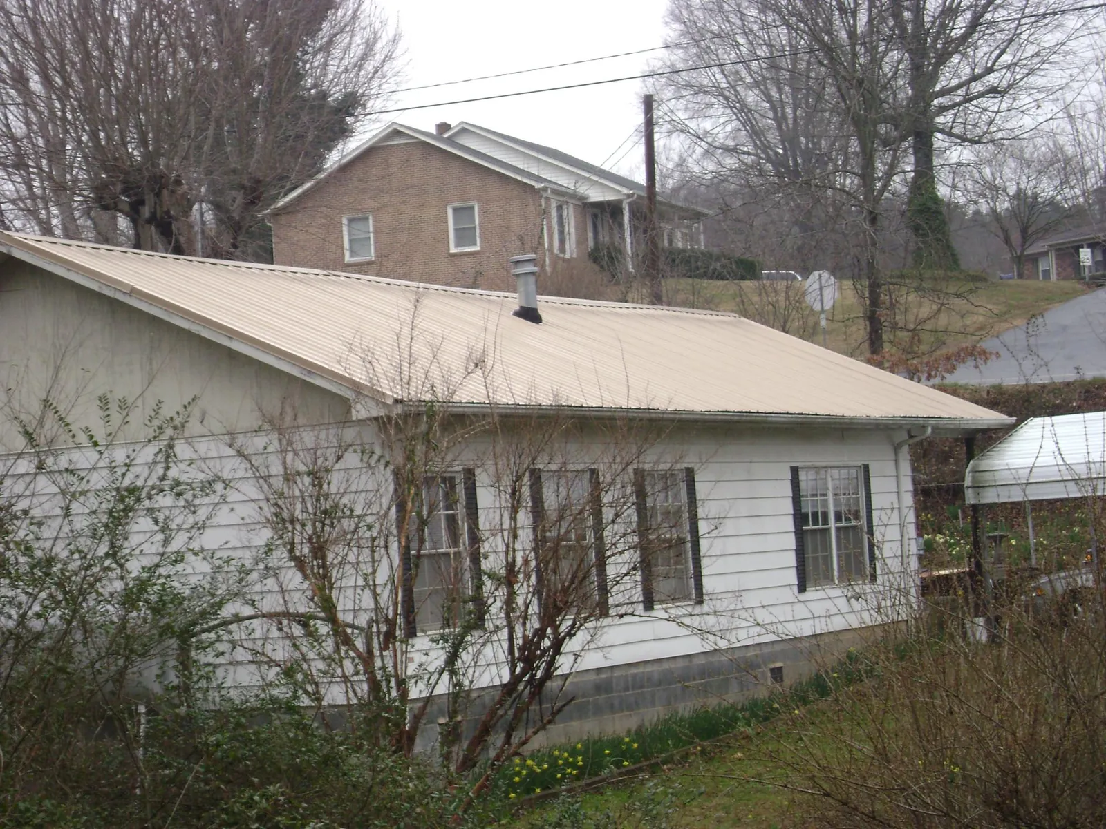 Tan metal roof on a white sided house set into a hillside — Commercial Roofing by Roofing Brothers in Ford