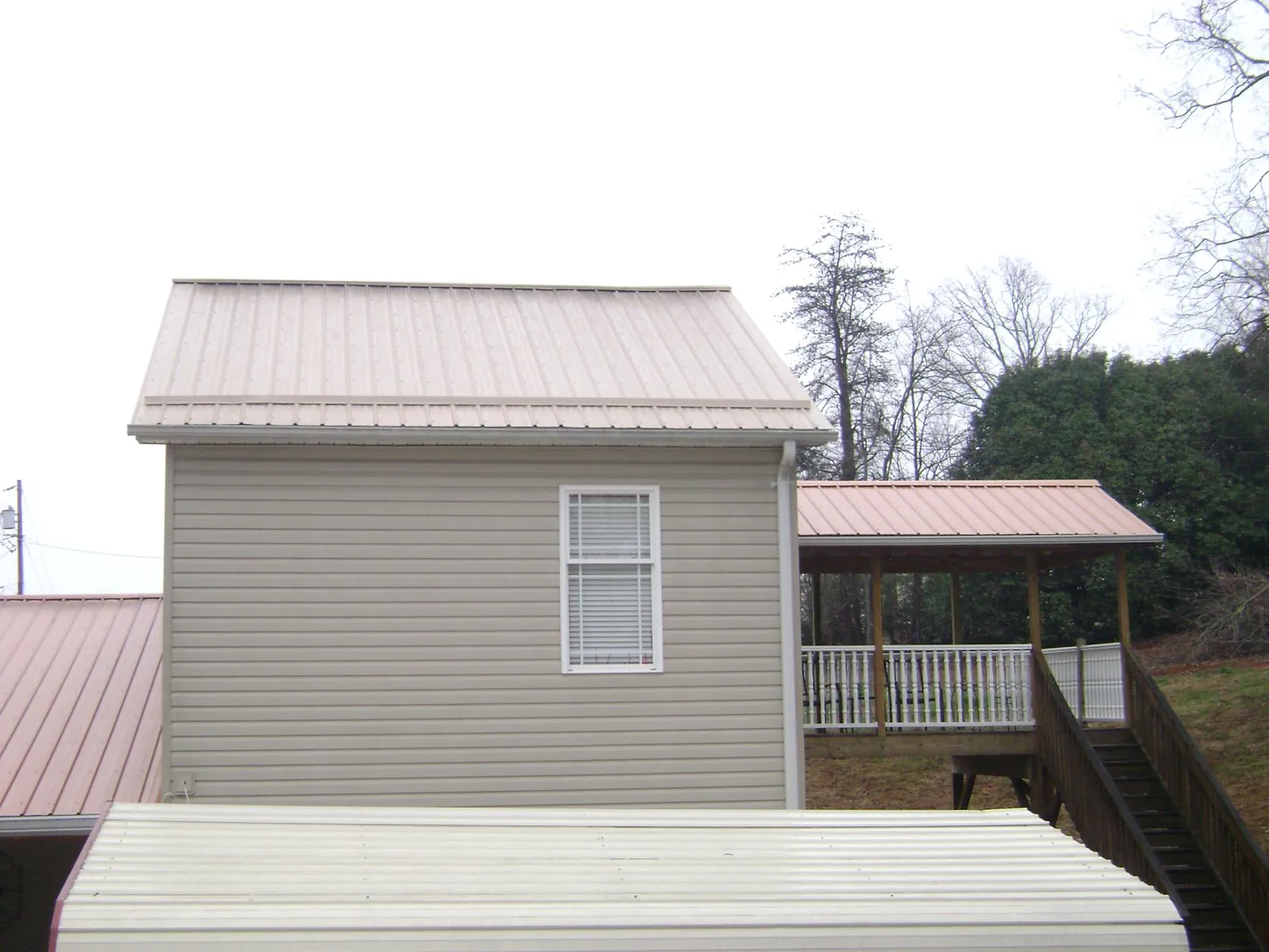 Tan metal roofs on a two story addition and attached porch, from a Roof Replacement job in Ford
